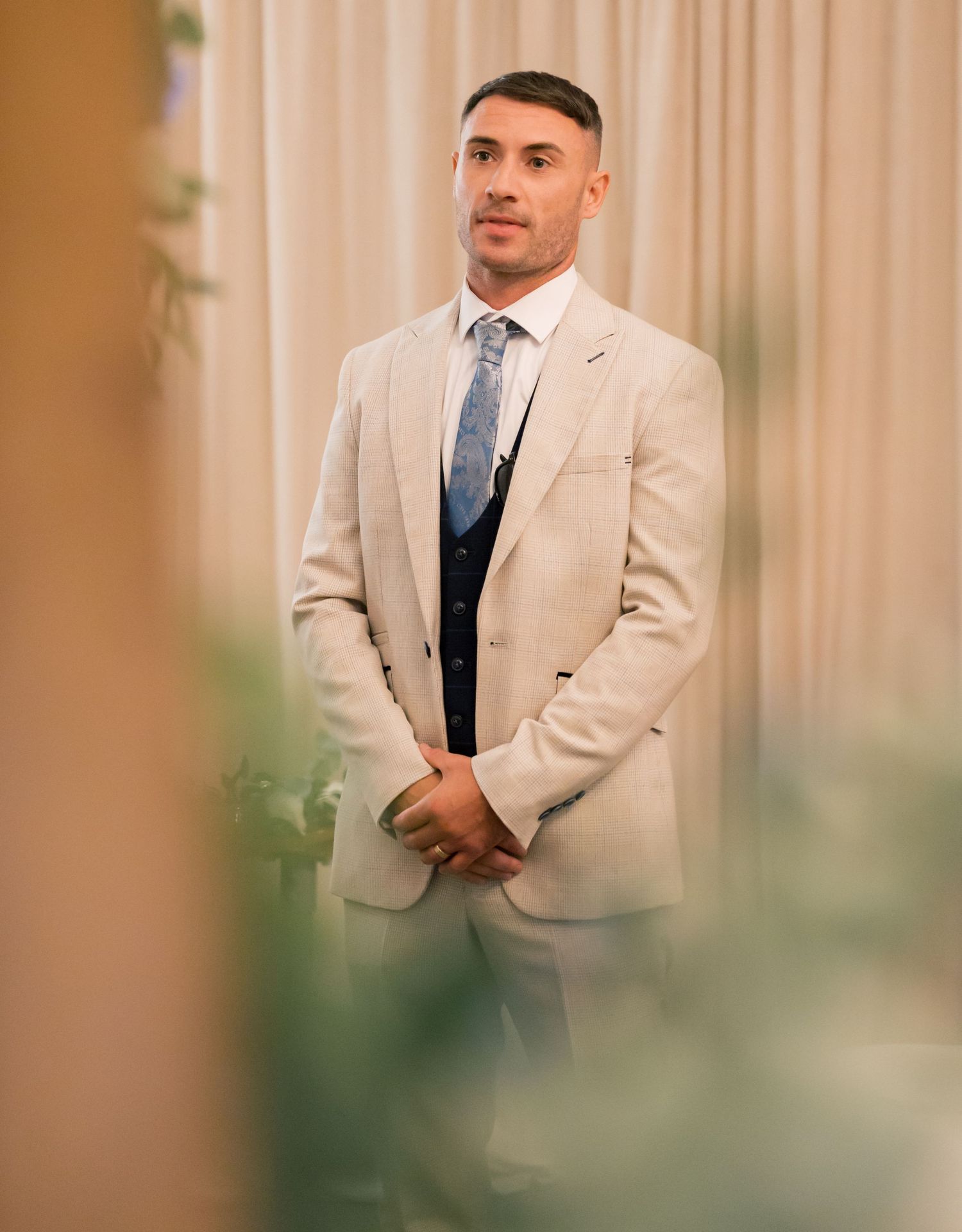 A row of men in beige suits and navy vests pose during a formal wedding event.