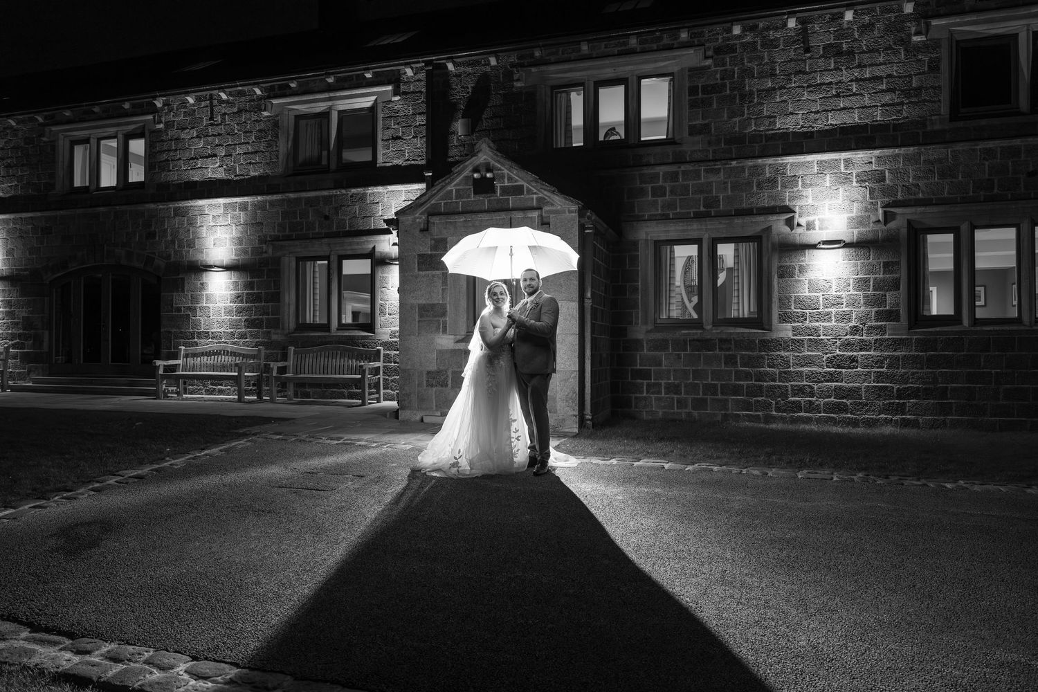 Atmospheric black and white wedding photo under an illuminated umbrella at night.