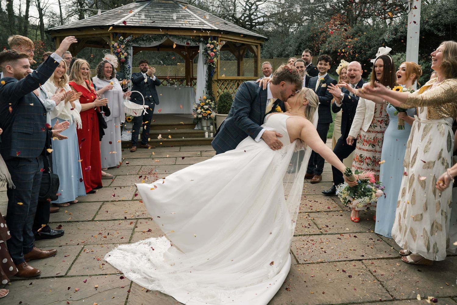 Bride and groom share a romantic dip kiss while wedding guests throw confetti outside a venue gazebo at Whitley Hall, Sheffield.