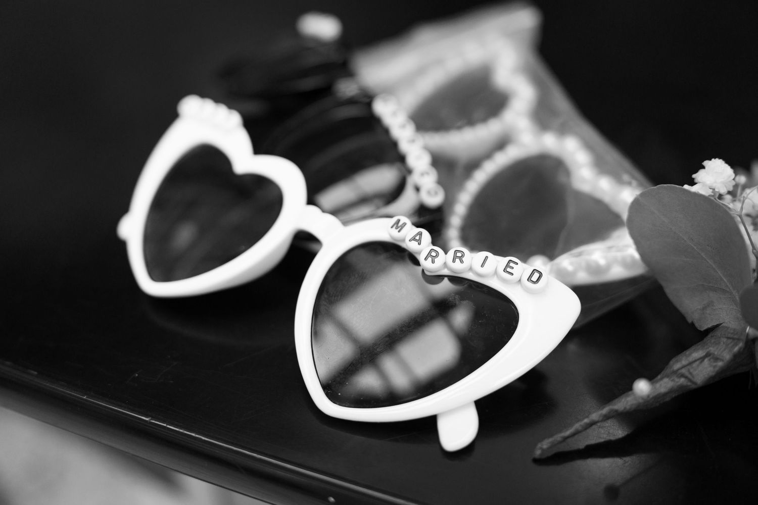 Black and white artistic detail shot of decorative sunglasses at a wedding.