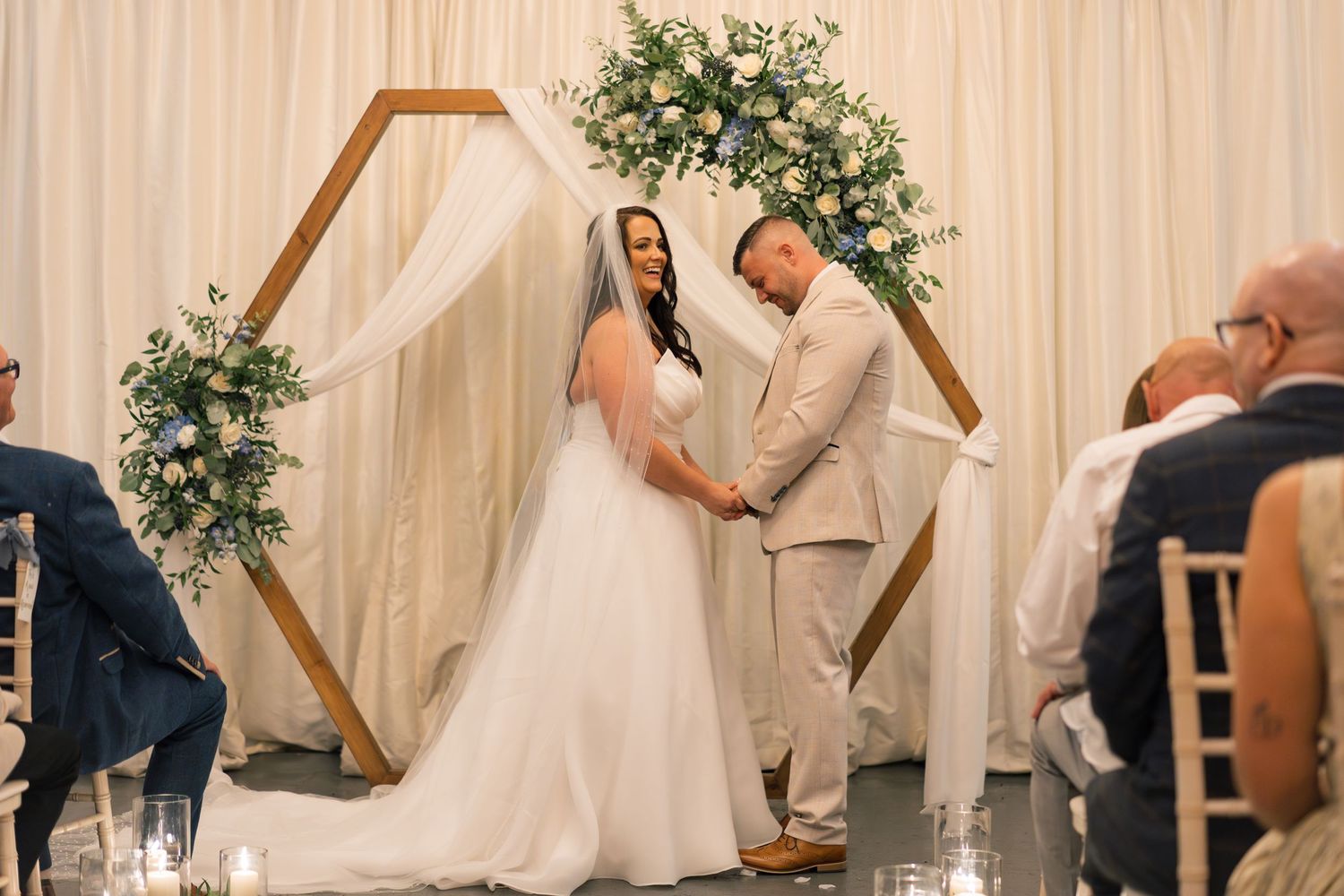 A series of wedding ceremony photos showing a couple exchanging rings under a floral arch with white draping.