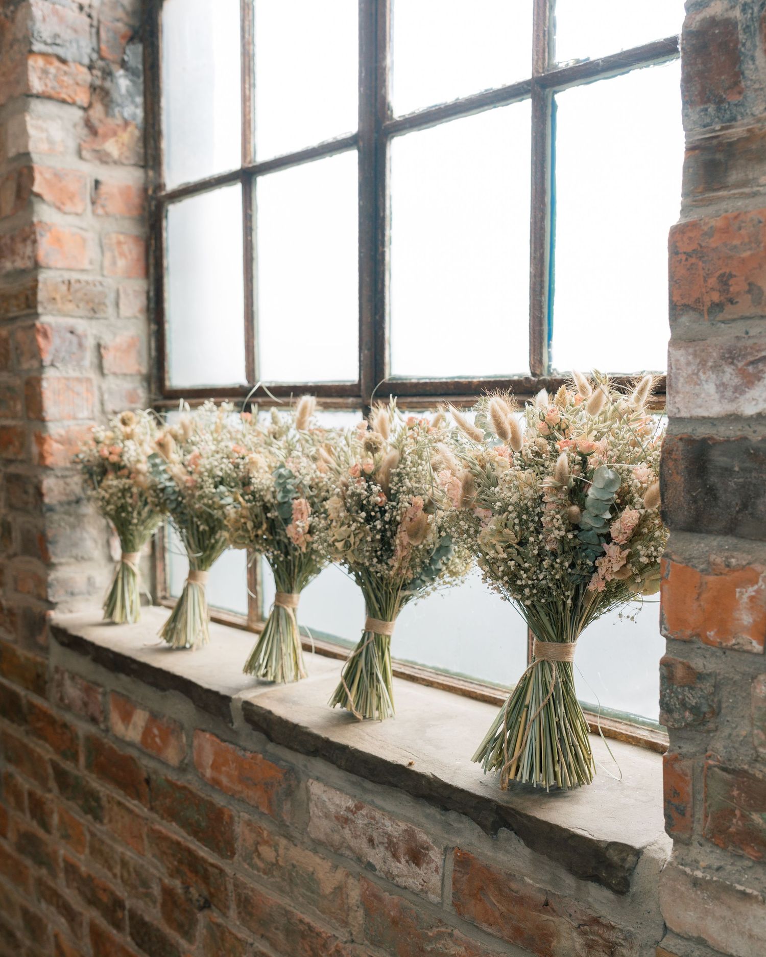 Dried flower bouquets displayed along rustic brick windowsills in natural light.