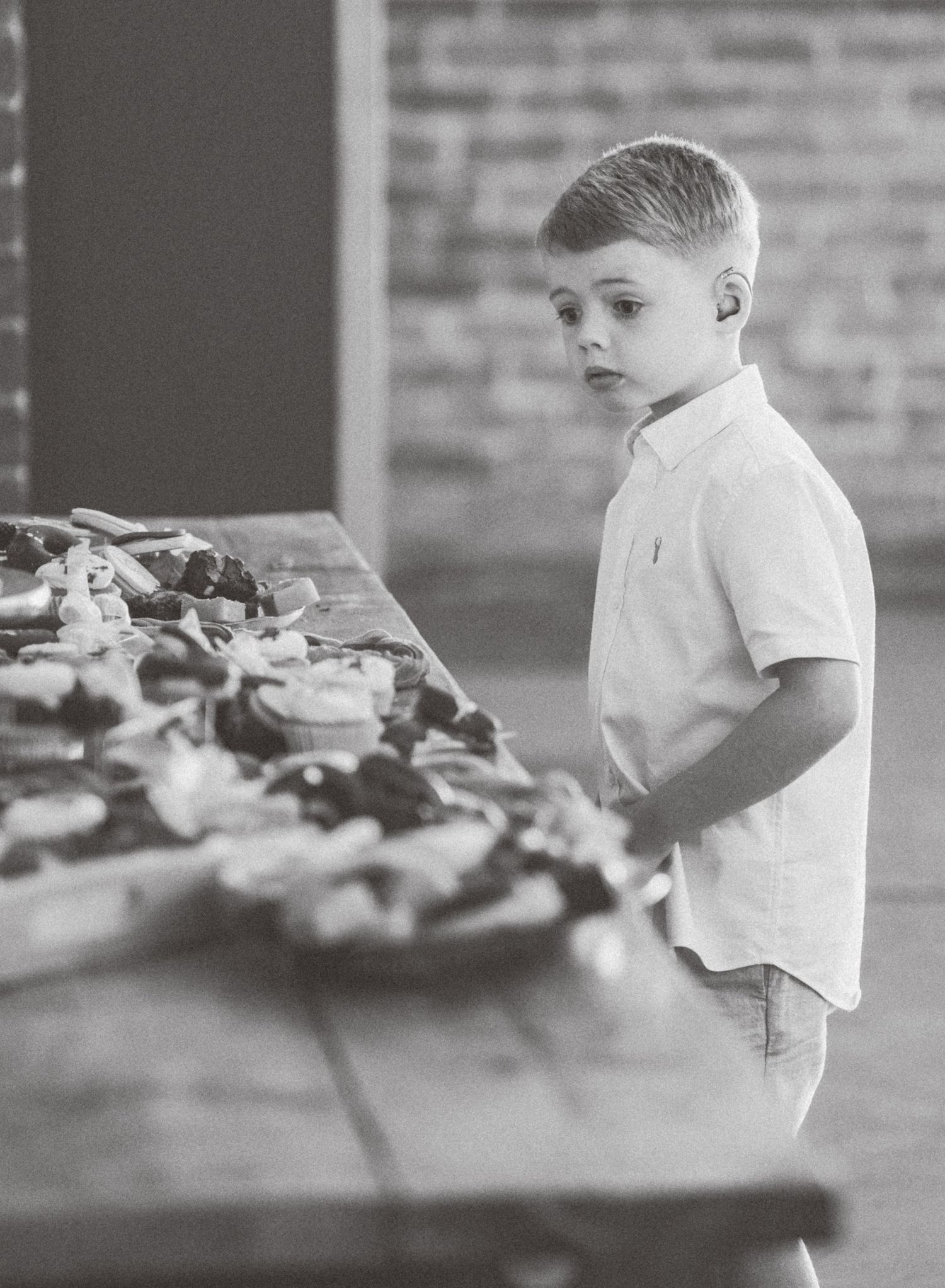 A young child in a white shirt stands near a table with refreshments at an event.