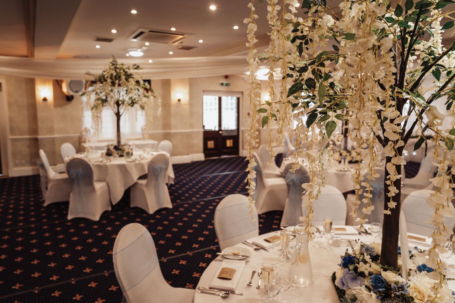 Luxurious ballroom decorated with white chairs and tall floral centerpieces for an elegant wedding reception.
