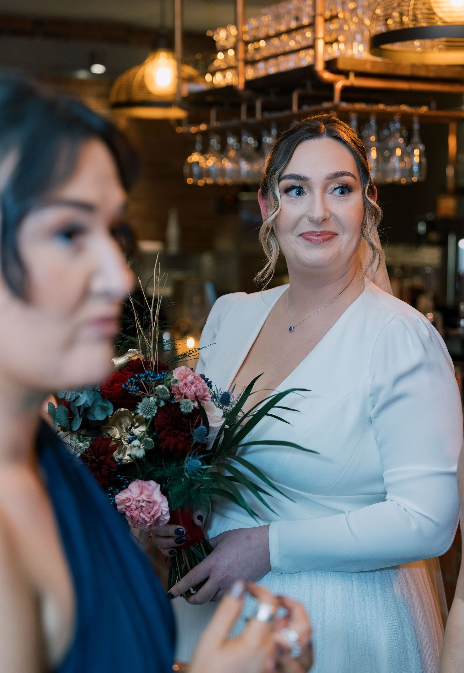 Wedding party members holding floral bouquets in bar setting.