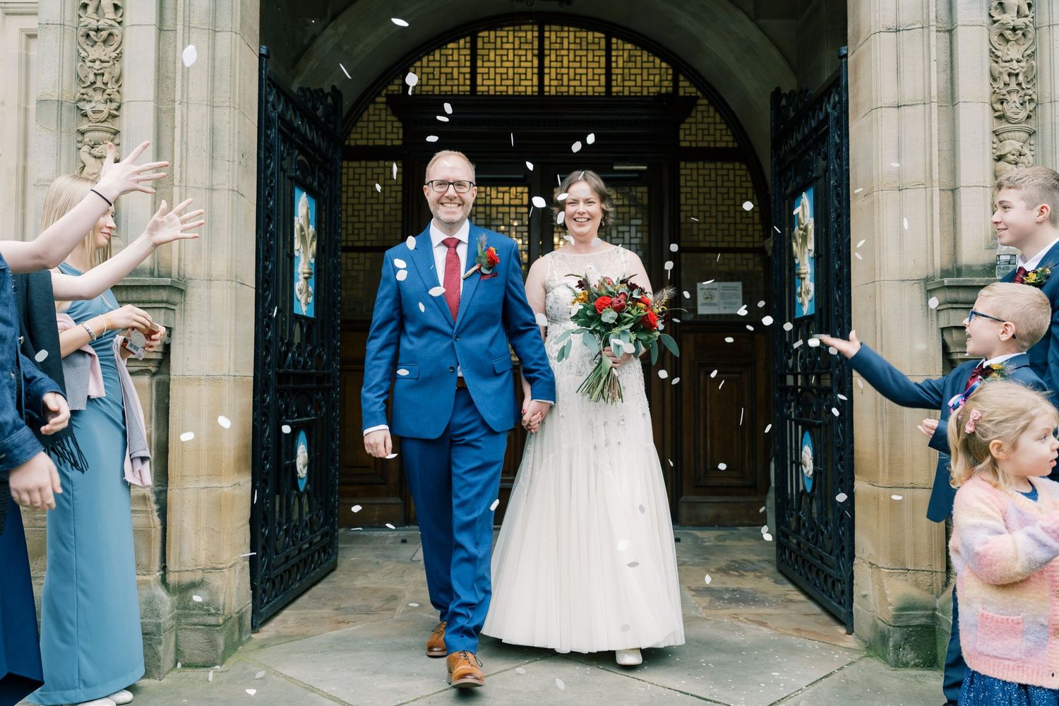 Wedding couple exits church while guests throw confetti during celebratory moment.