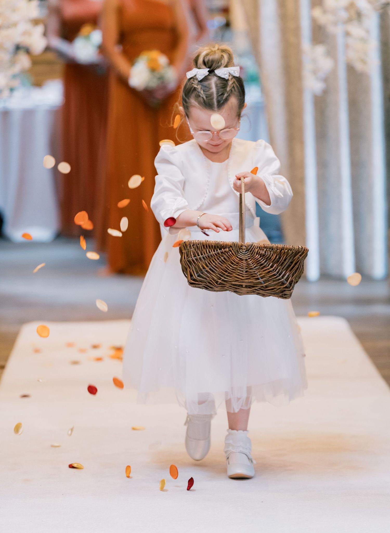 A flower girl in a white dress scatters rose petals on a light colored floor during a wedding ceremony at Spicer Manor, Sheffield.