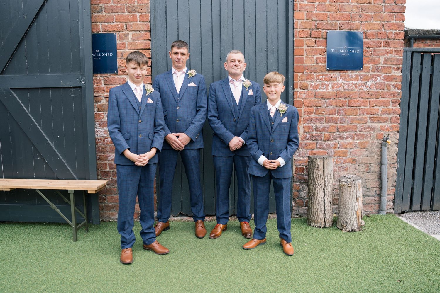 Groomsmen in navy suits pose together against a brick wall backdrop at a wedding venue.
