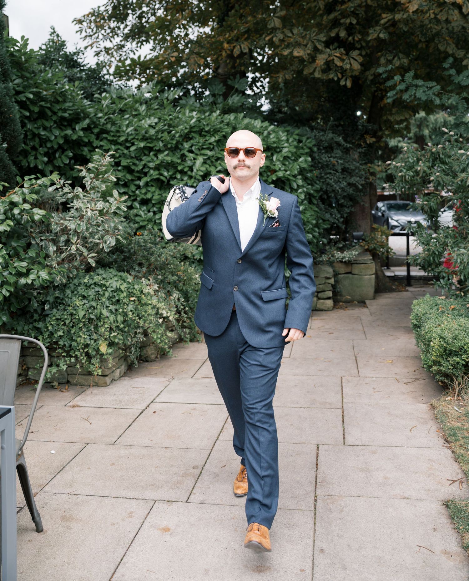 Person in navy suit walking playfully along stone pathway surrounded by greenery.
