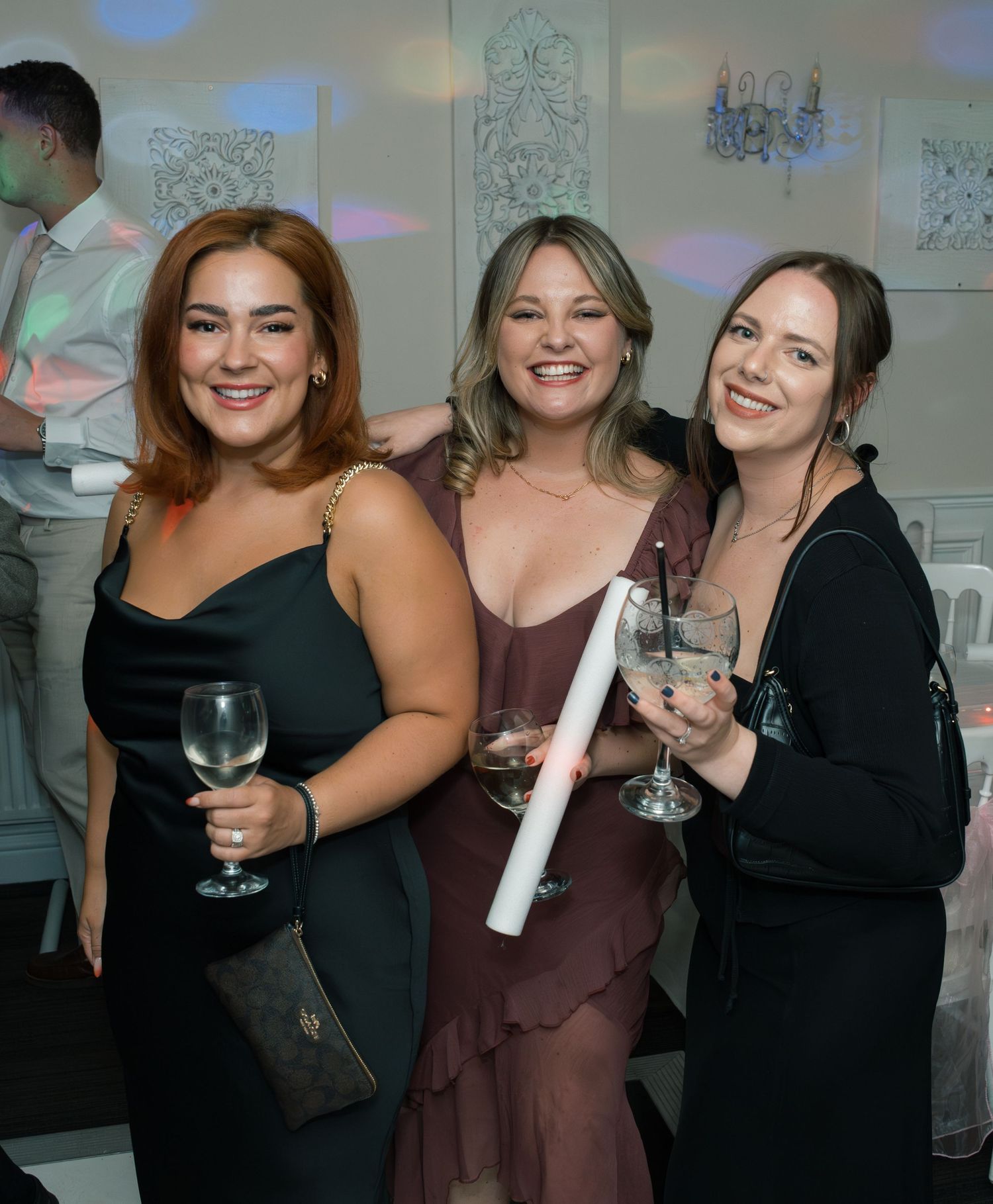 Friends in dark formal attire enjoying drinks and conversation at a wedding reception.