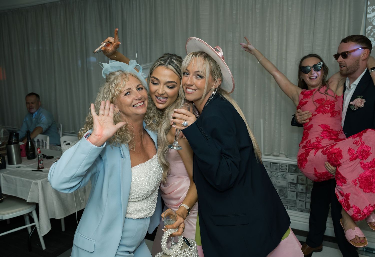 Wedding guests celebrating and dancing together at a reception with decorative draping in the background.