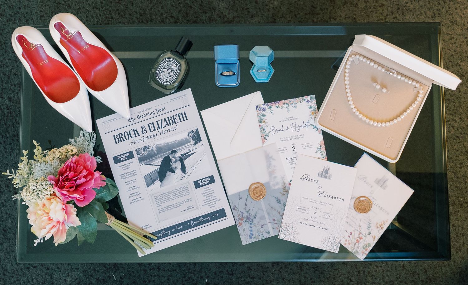 Wedding day details including red shoes, invitations and jewelry displayed on glass surface.
