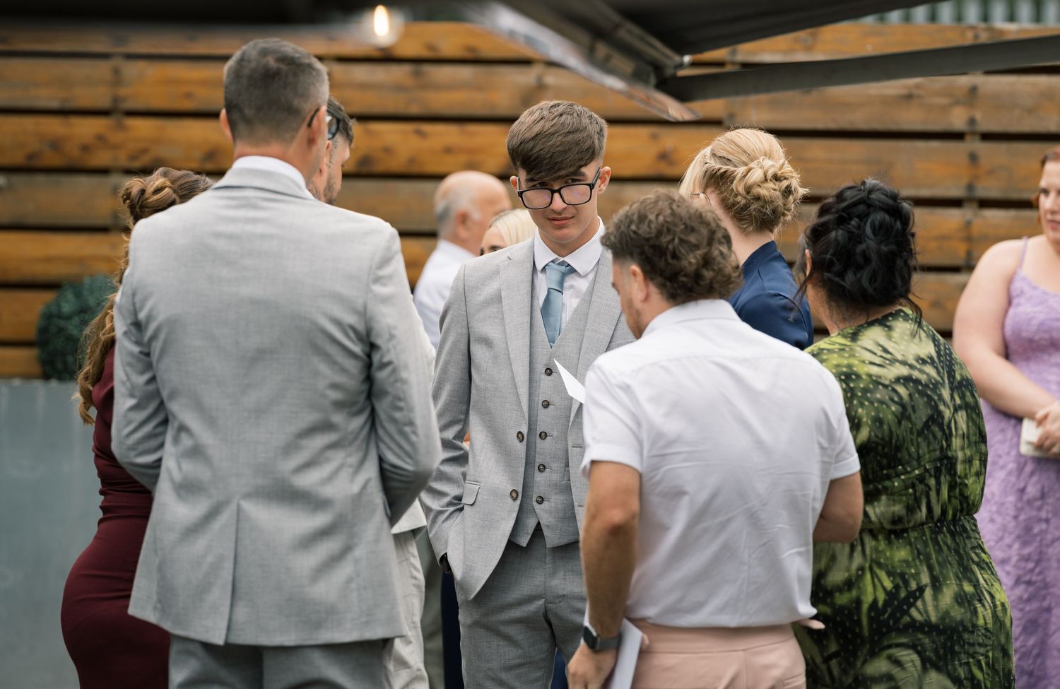 Wedding party members in gray suits gather in conversation during an outdoor celebration.