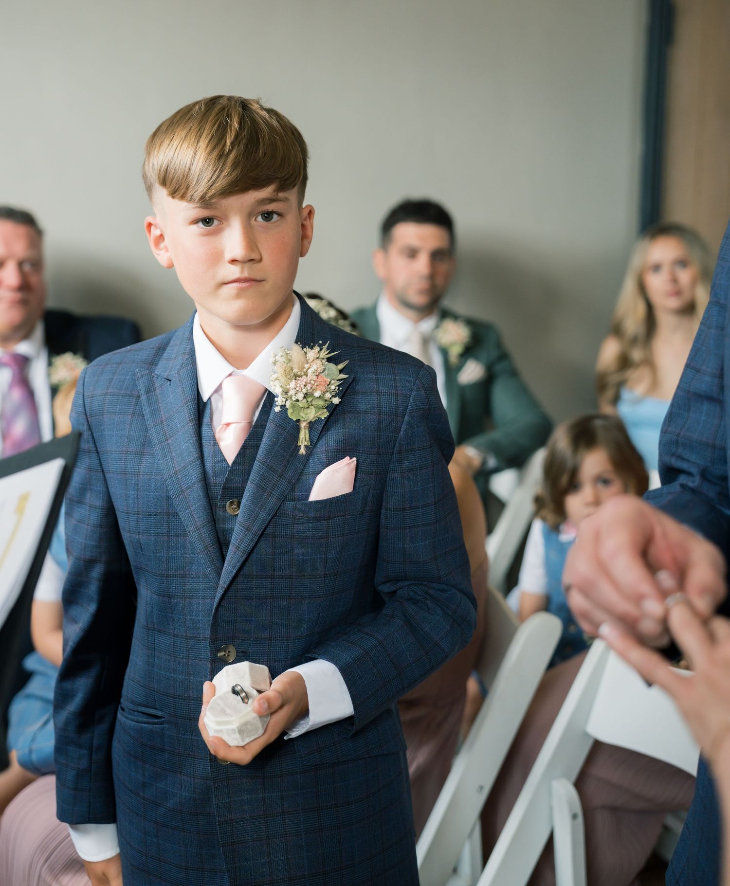 Ring bearer in navy suit stands in wedding ceremony venue.