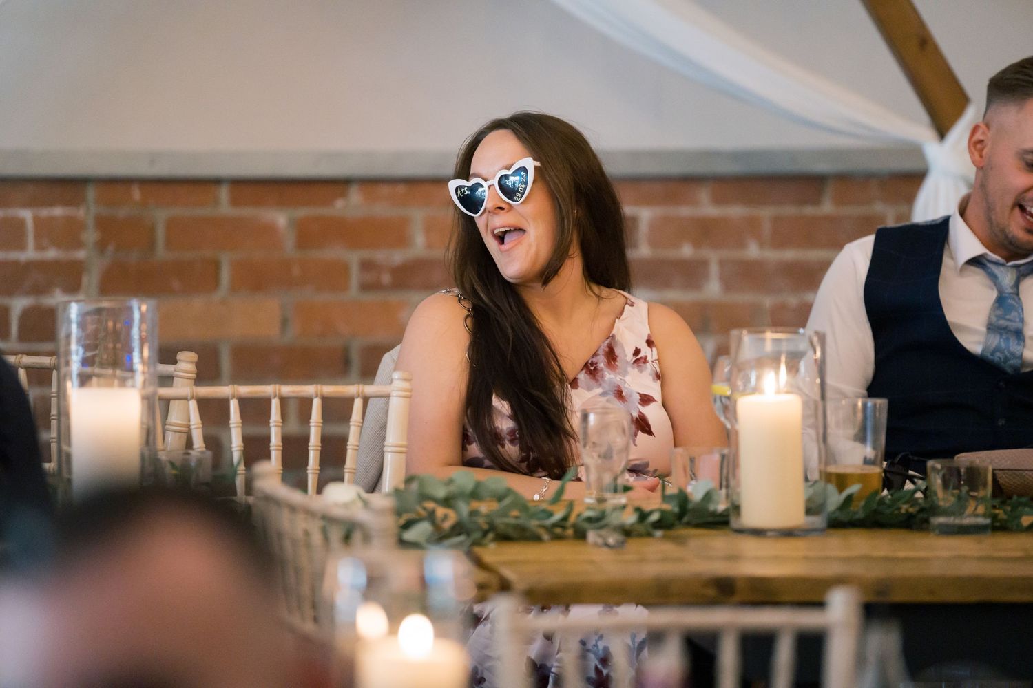 Wedding reception table setting with candles and greenery against exposed brick wall.
