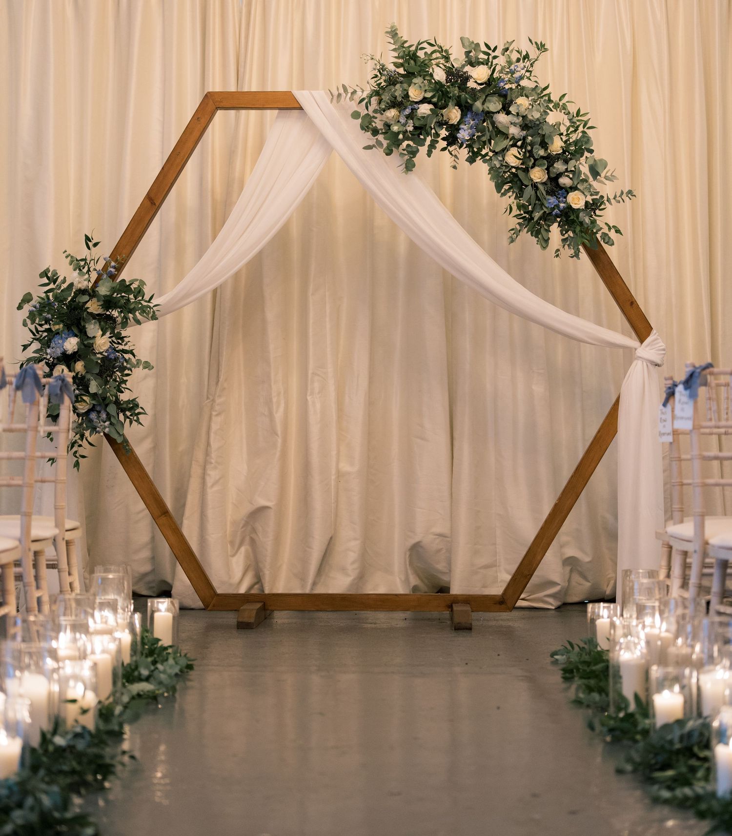 Elegant wedding venue interior with white draping, wooden beams, and floral arrangements.