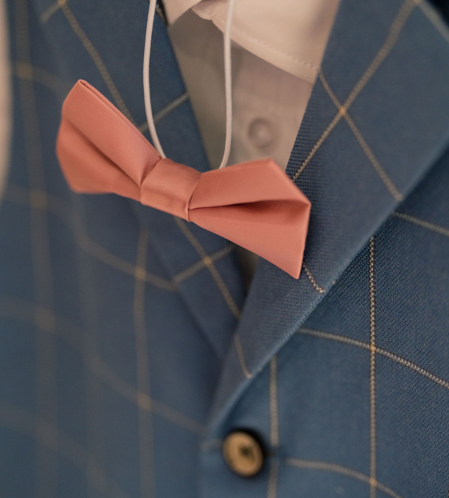 Close-up detail of a blue suit jacket with a coral pink bow tie accent.