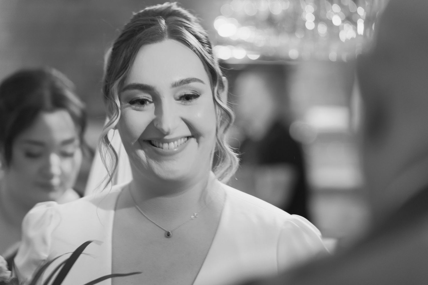 A woman with dark hair in a satin dress smiles as she gets her makeup done at a beauty counter.