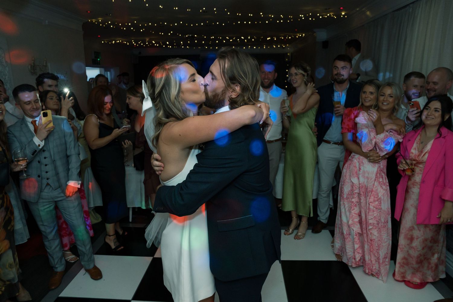 Lively dance floor scene at wedding reception with guests enjoying the celebration under twinkle lights.