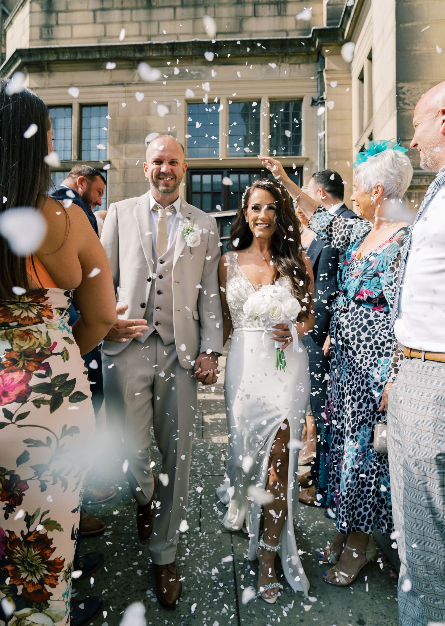 Wedding celebration with confetti shower outside stone building entrance.