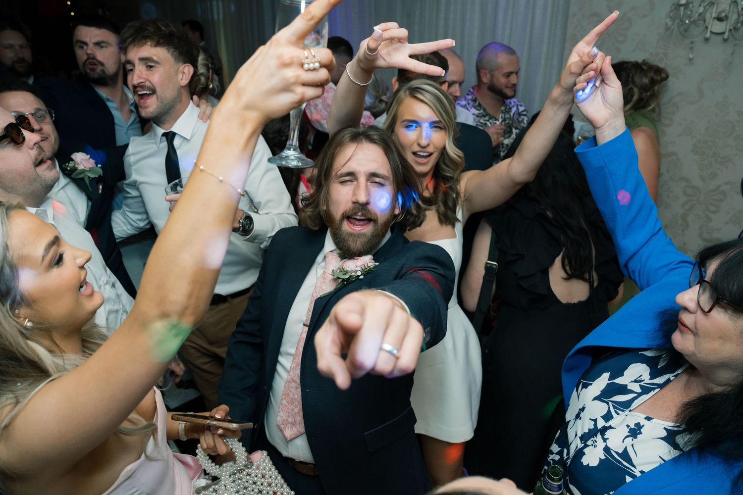 Energetic dance floor scene at wedding reception with guests celebrating.