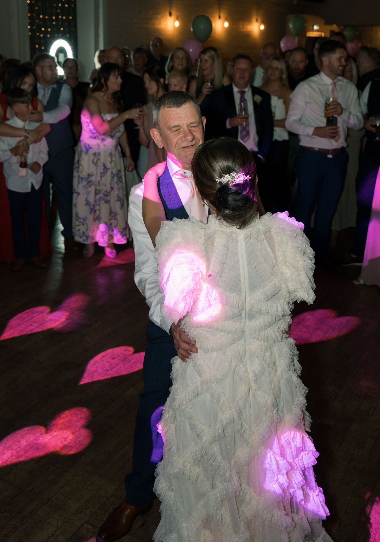 Wedding reception dance floor lit with pink and purple lights as couples dance together.