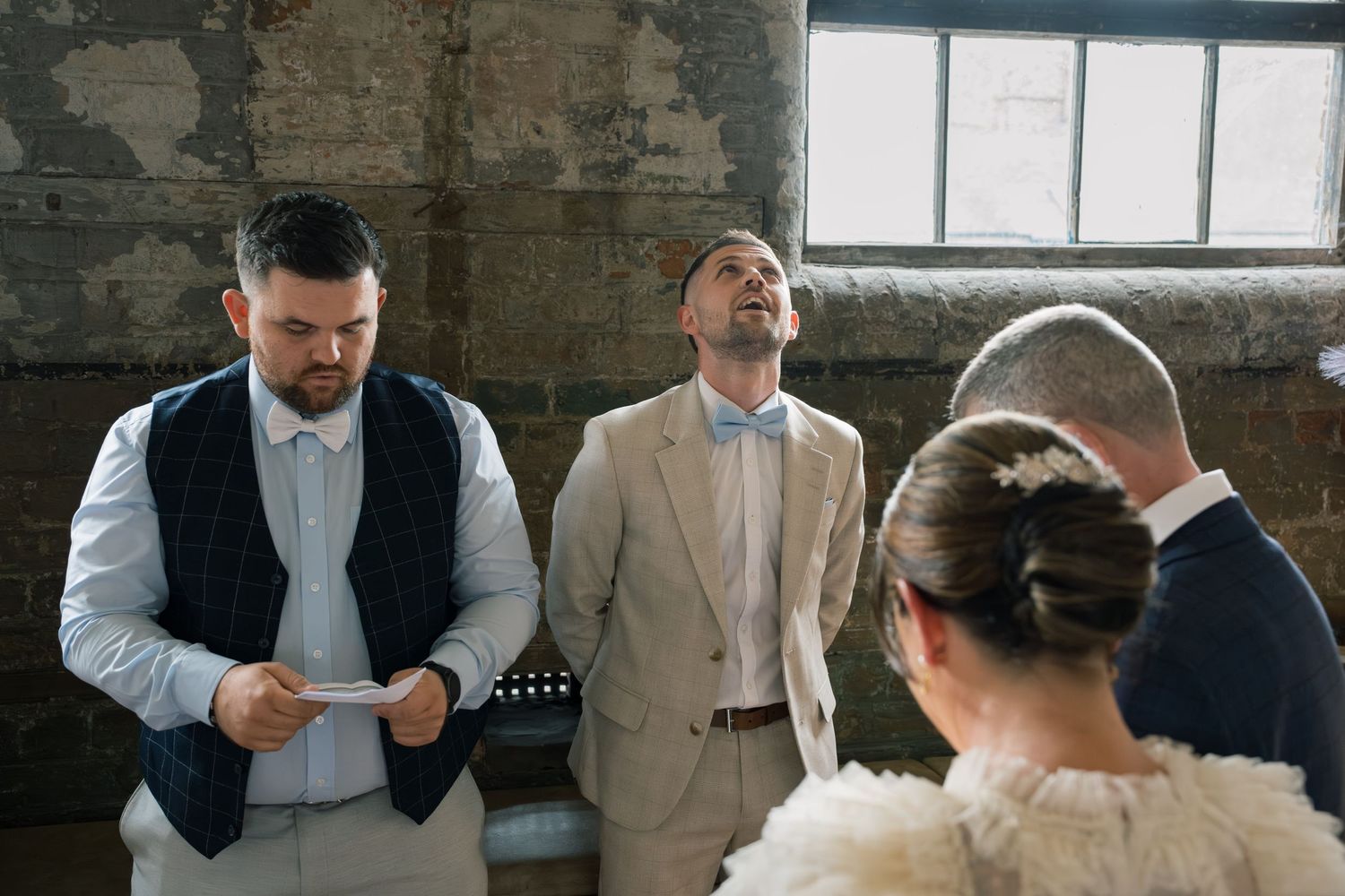 Wedding party members share candid moments in formal attire against a brick wall backdrop.