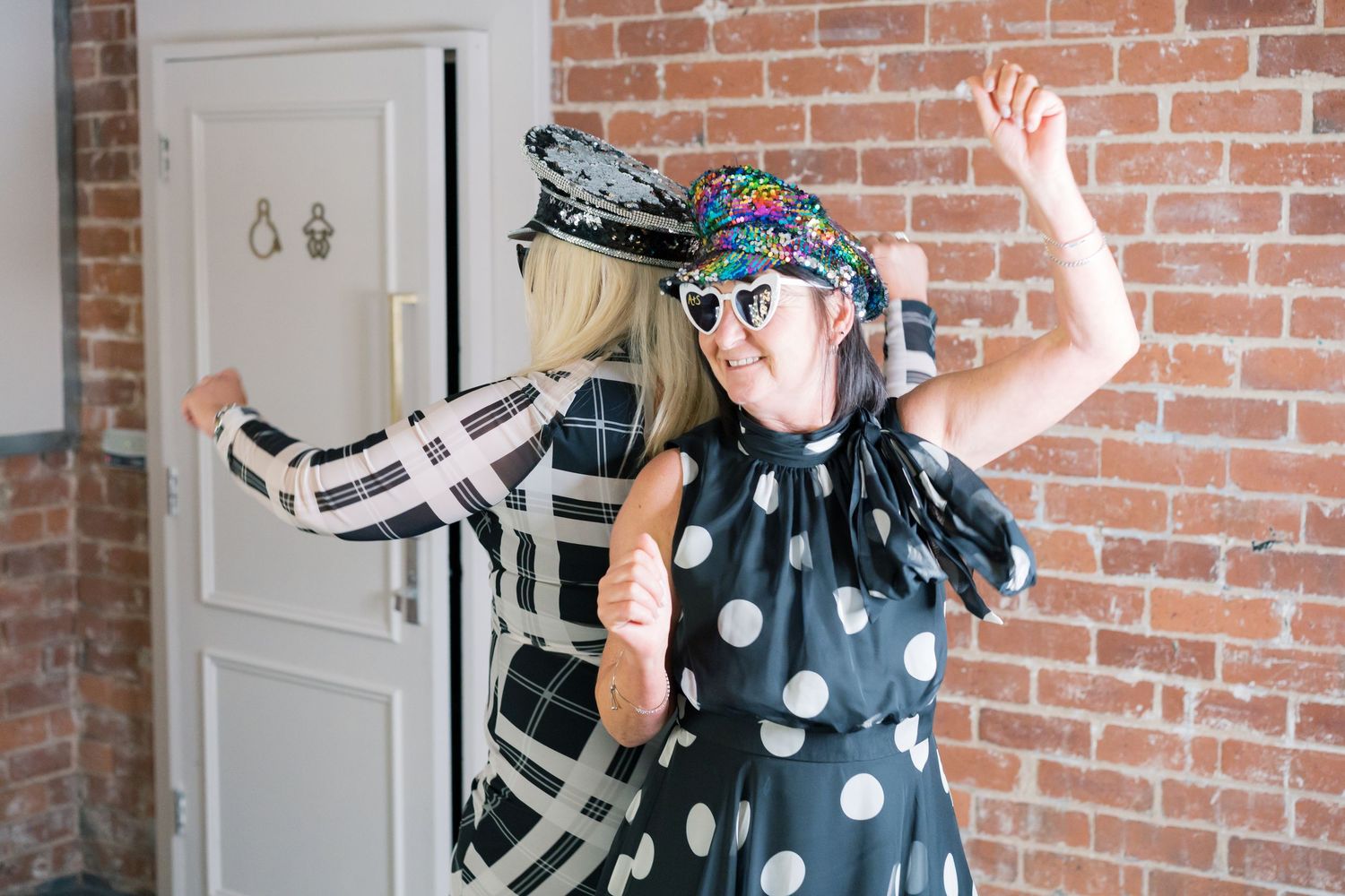 Person in polka dot dress striking playful pose against brick wall at party.