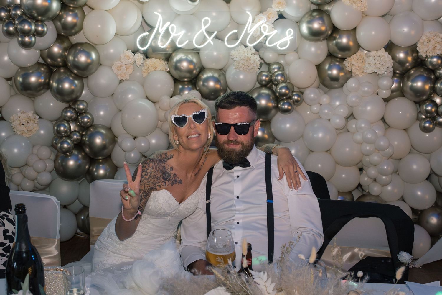 Newlyweds pose in front of a white and silver balloon arch with a Mr & Mrs neon sign at their wedding reception in Leeds