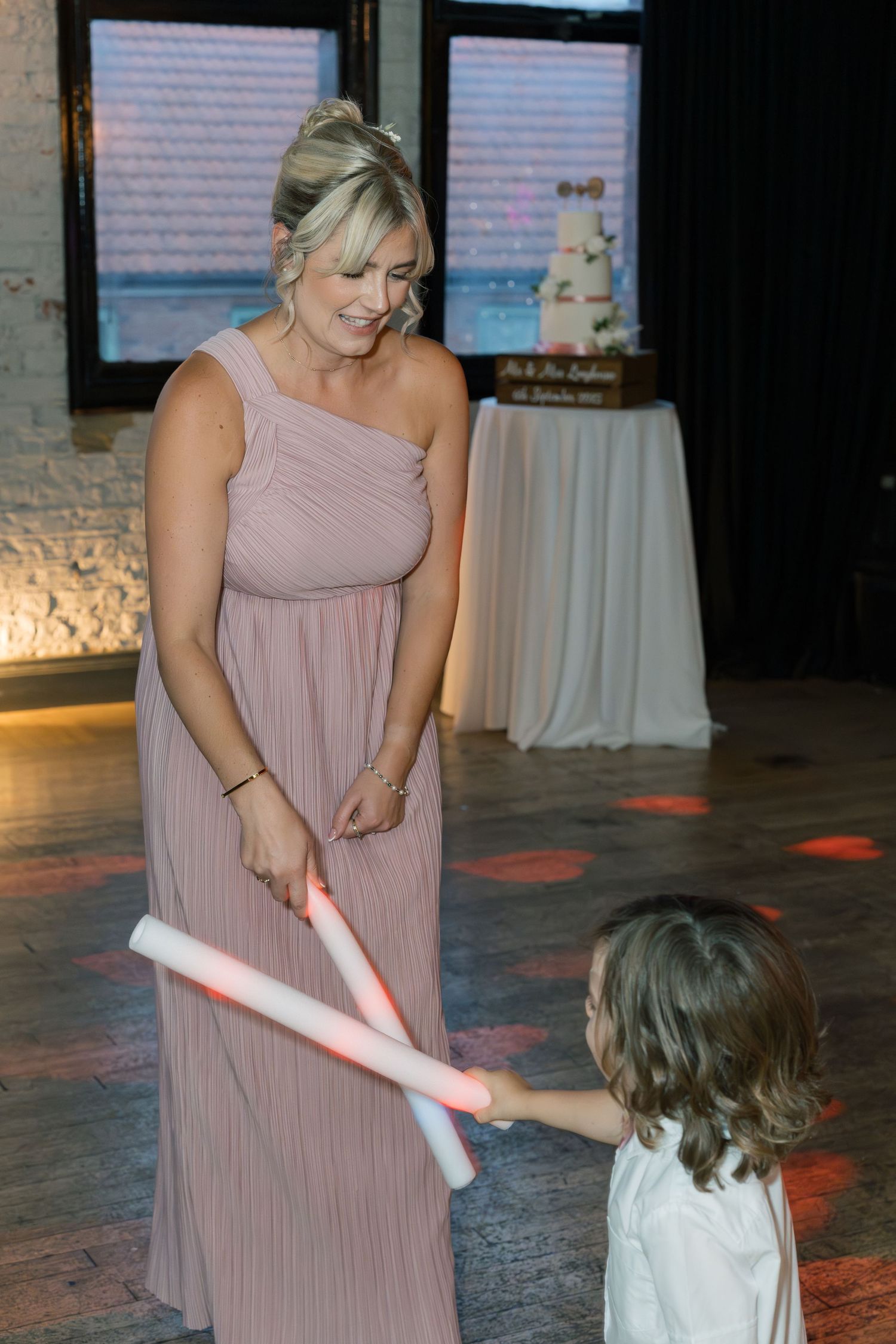 A person in a pink dress plays with light-up wands on a dark dance floor.