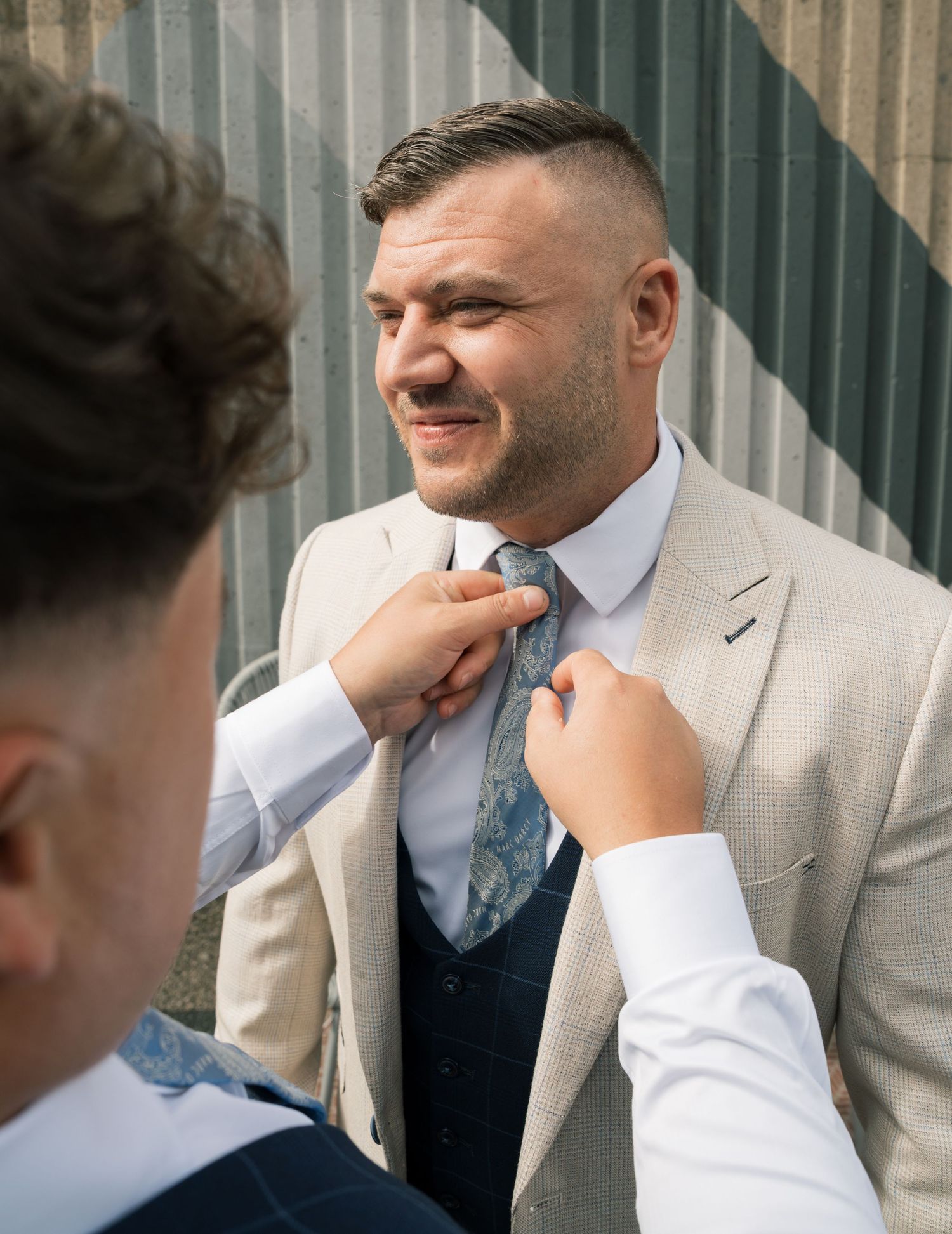 A sequence of photos showing someone adjusting a light blue tie against a navy suit with a striped backdrop.