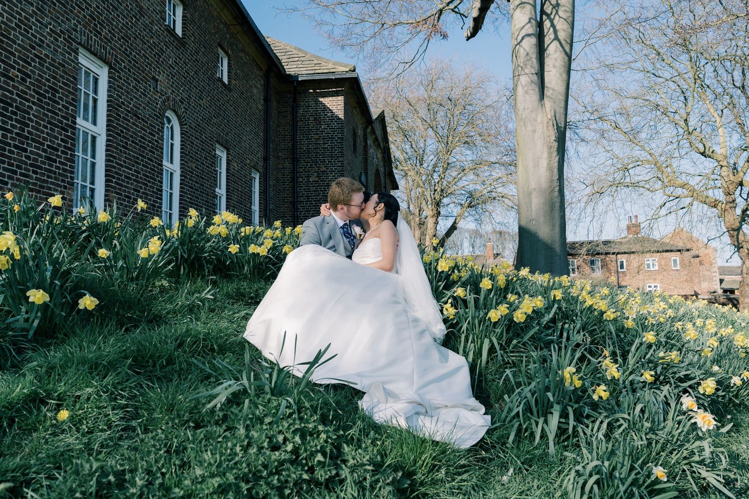 A beautiful spring scene with a white wedding gown on a grassy hillside dotted with blooming daffodils beside a stone building.