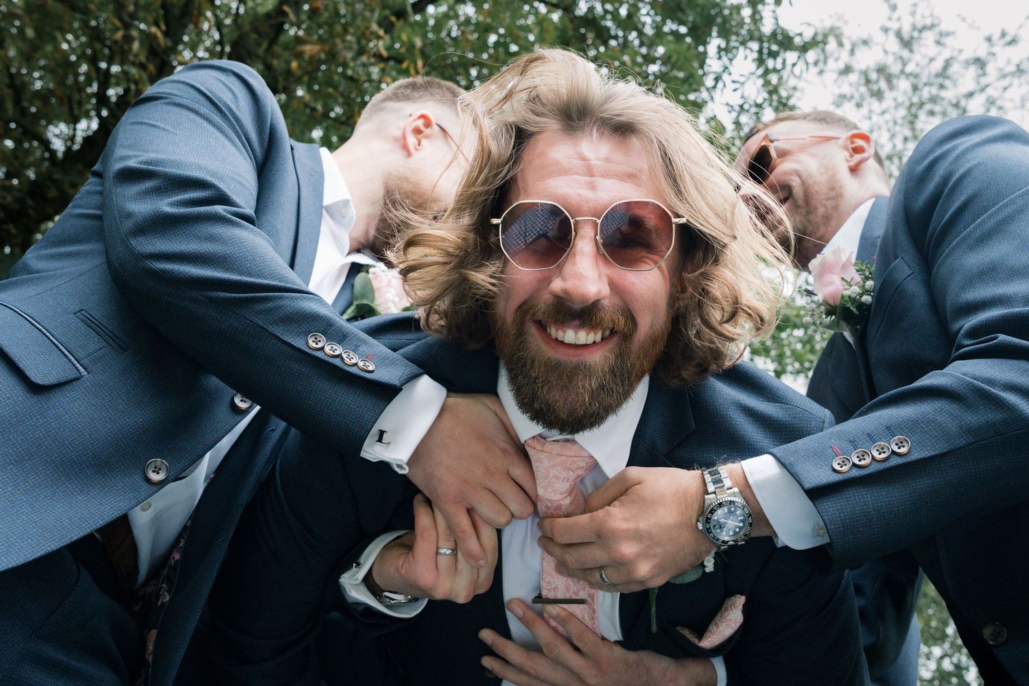 Groomsmen in navy suits playfully pose together for a candid photo outdoors.