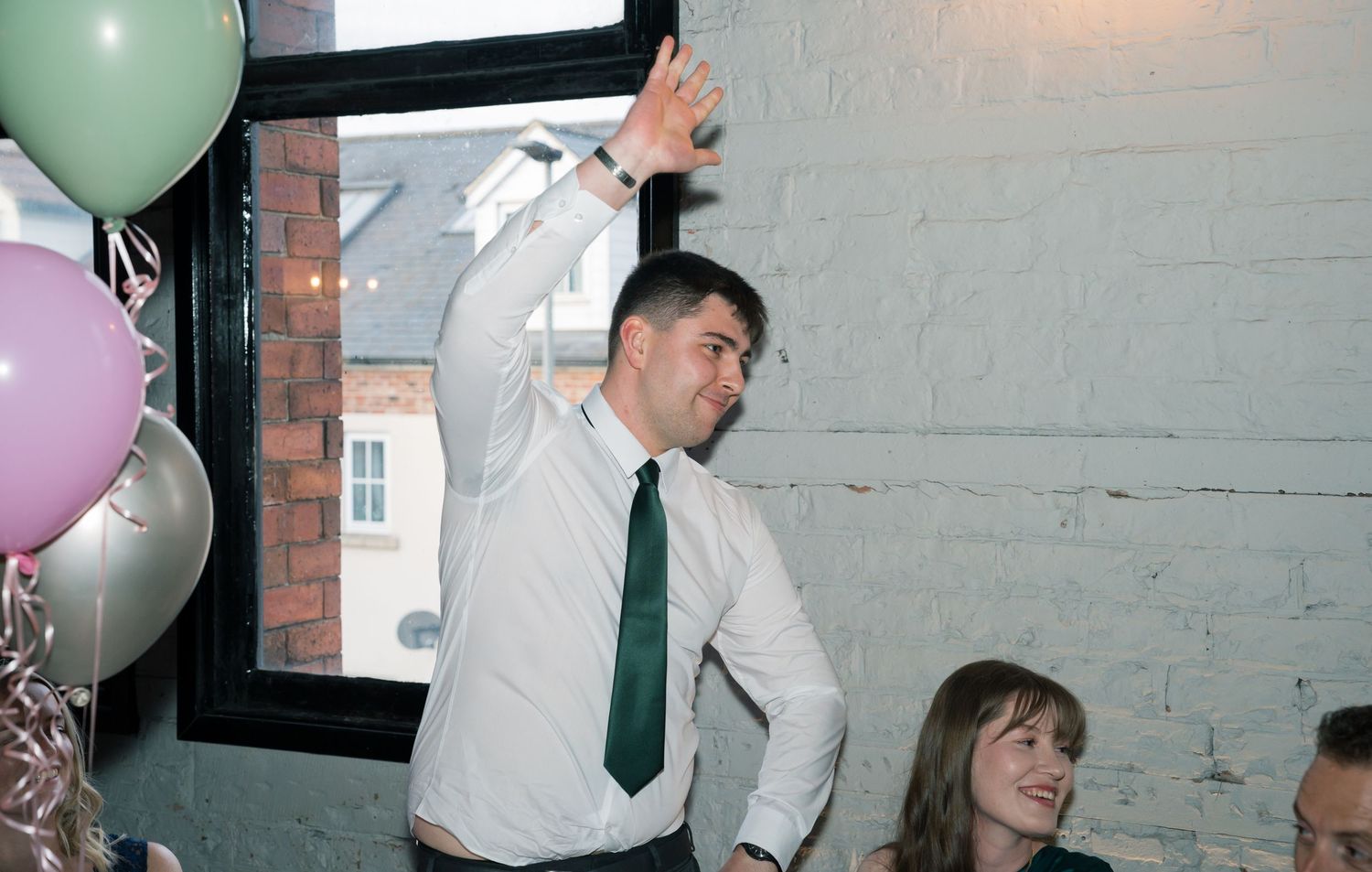 Wedding celebration with green and pink balloons decorating an industrial-style venue space.