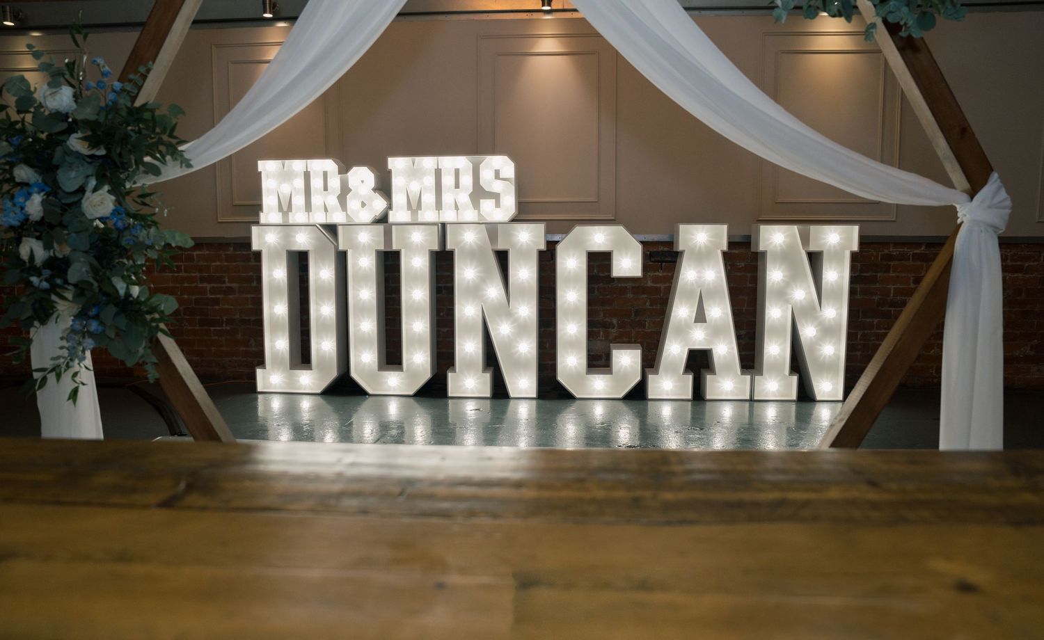 Illuminated marquee letters spelling out names at a wedding reception against a dark background.