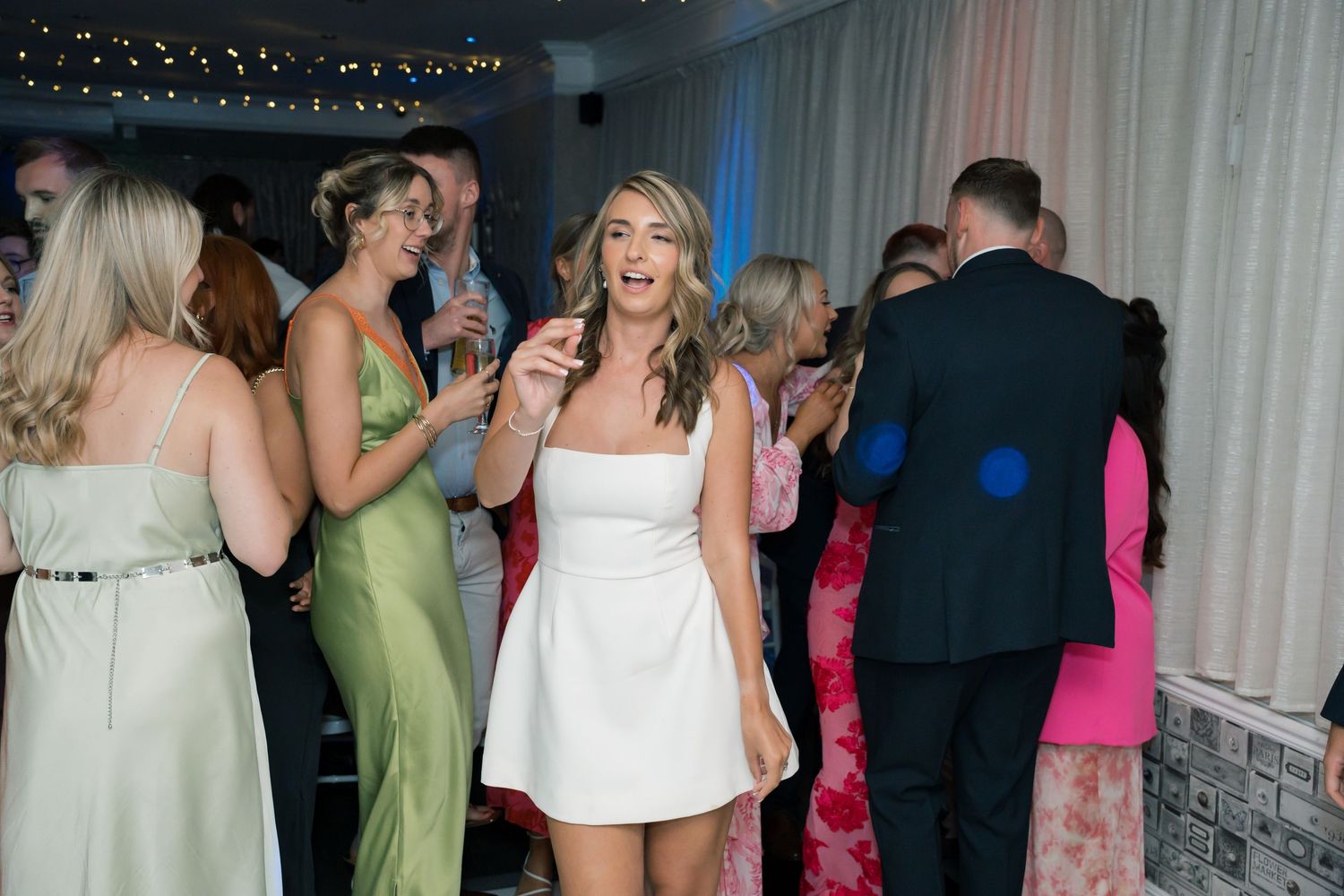 Wedding reception dance floor filled with guests under string lights.