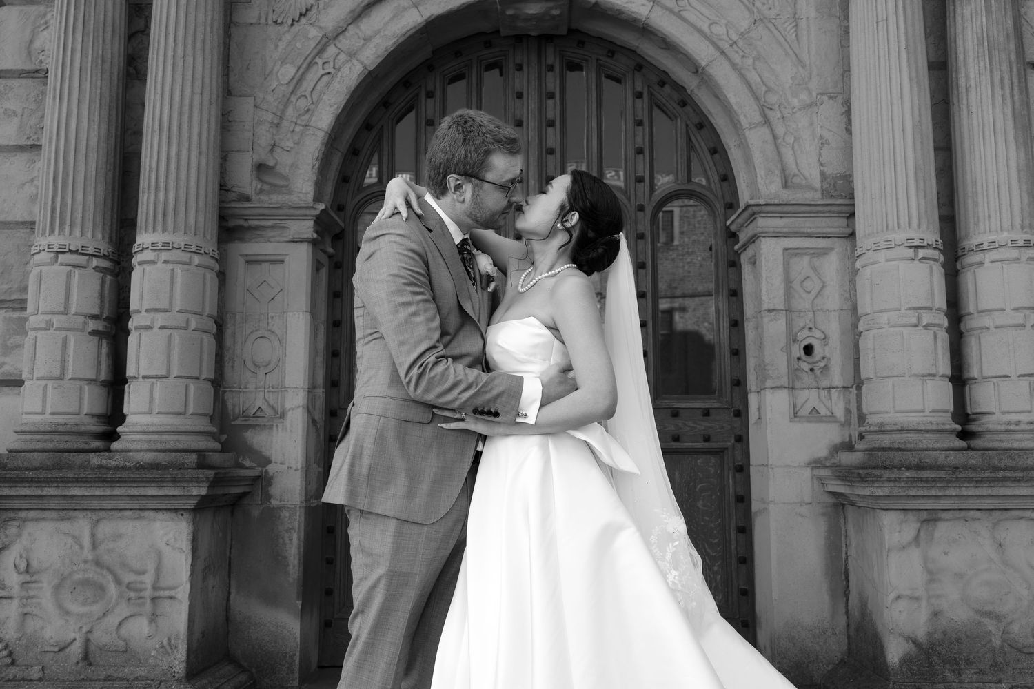 A romantic black and white wedding photo of a couple sharing a tender moment in front of an ornate stone church entrance.