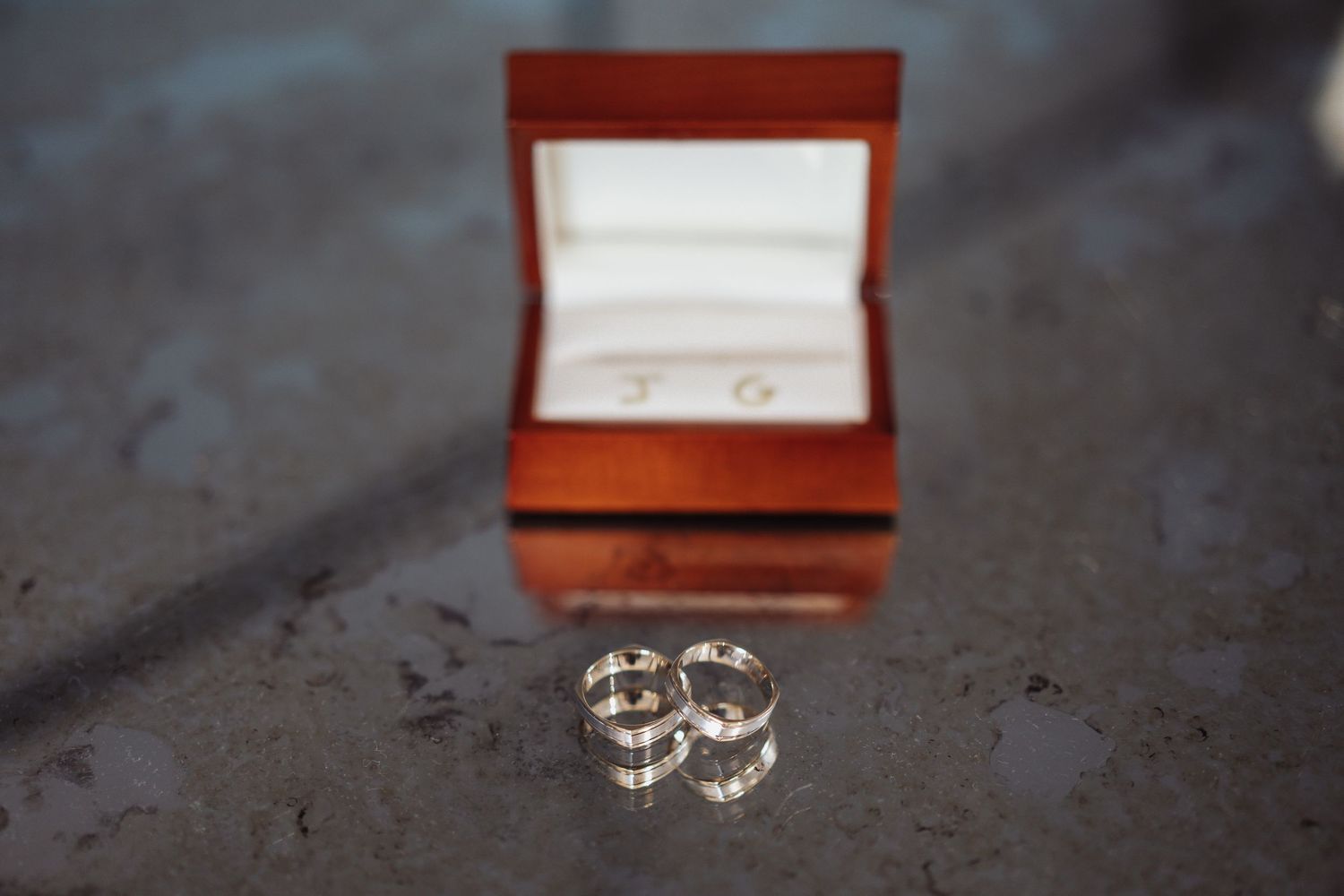 A silver wedding ring set rests in an elegant red jewelry box on a dark surface.