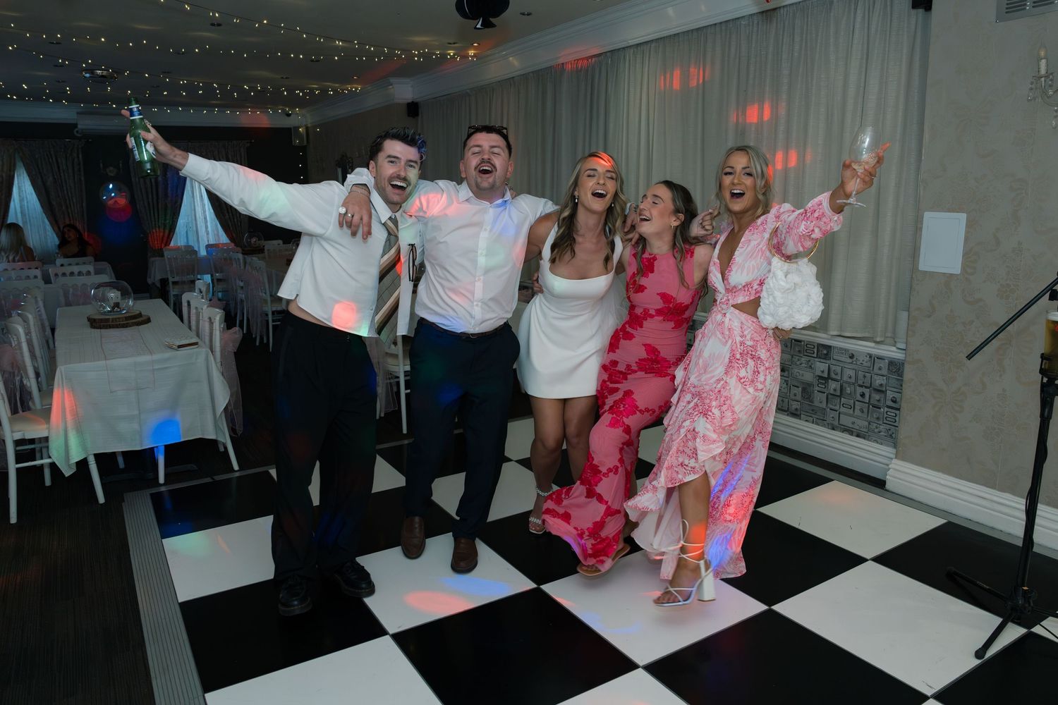 Wedding party dancing and celebrating in an indoor venue with white floors.