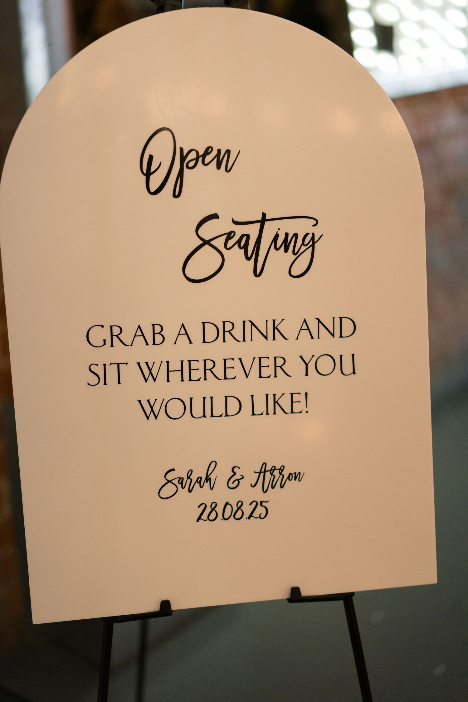 Wedding seating sign reads 'Grab a drink and sit wherever you would like' in elegant script.