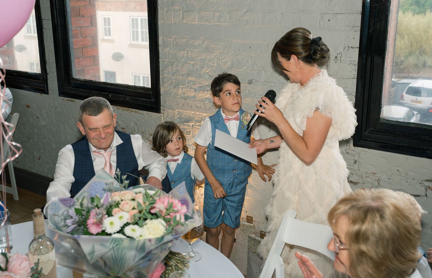 Wedding reception scene with guests gathered at tables in rustic venue setting.