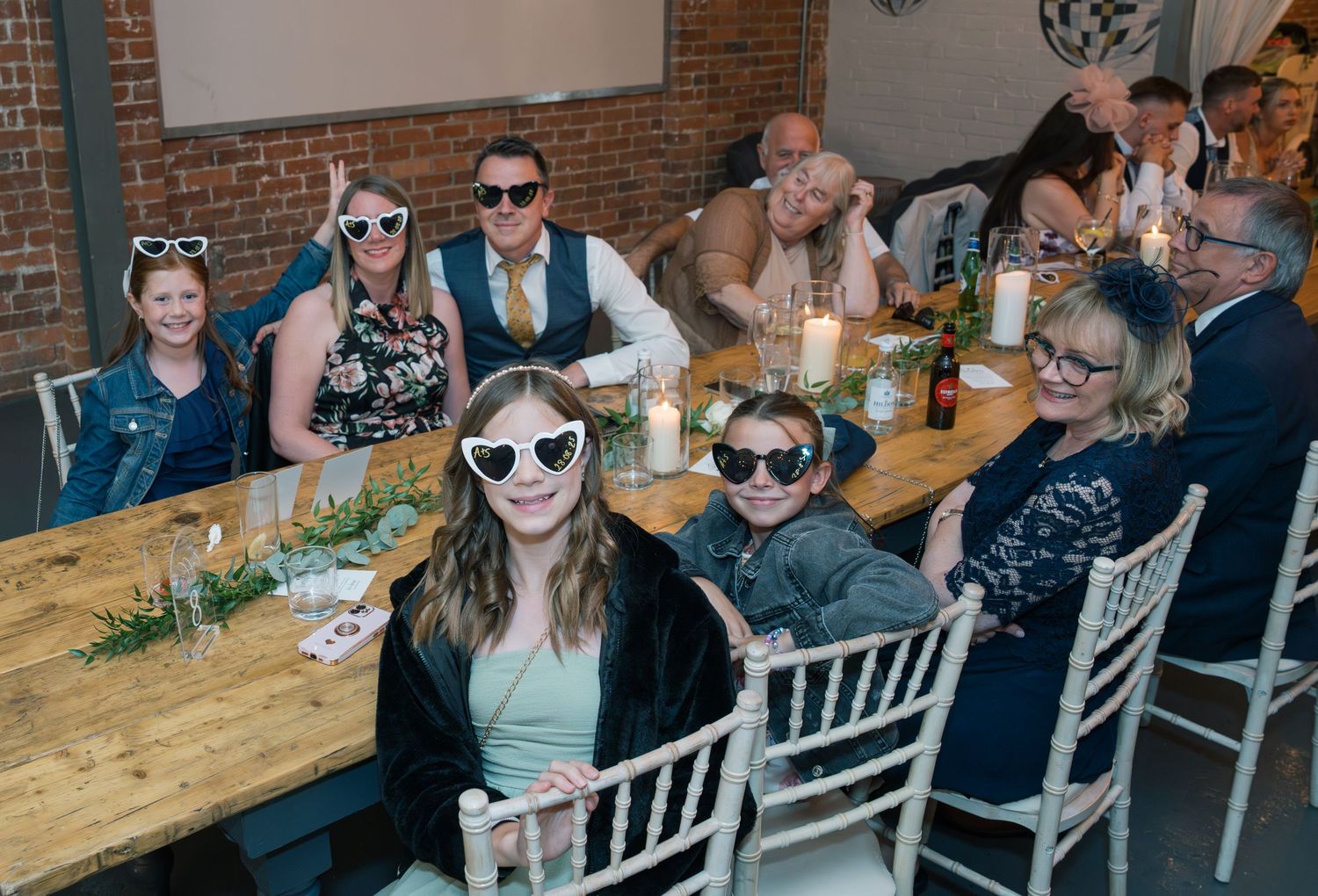 Wedding guests seated at long wooden tables in an industrial-style venue with exposed brick walls.