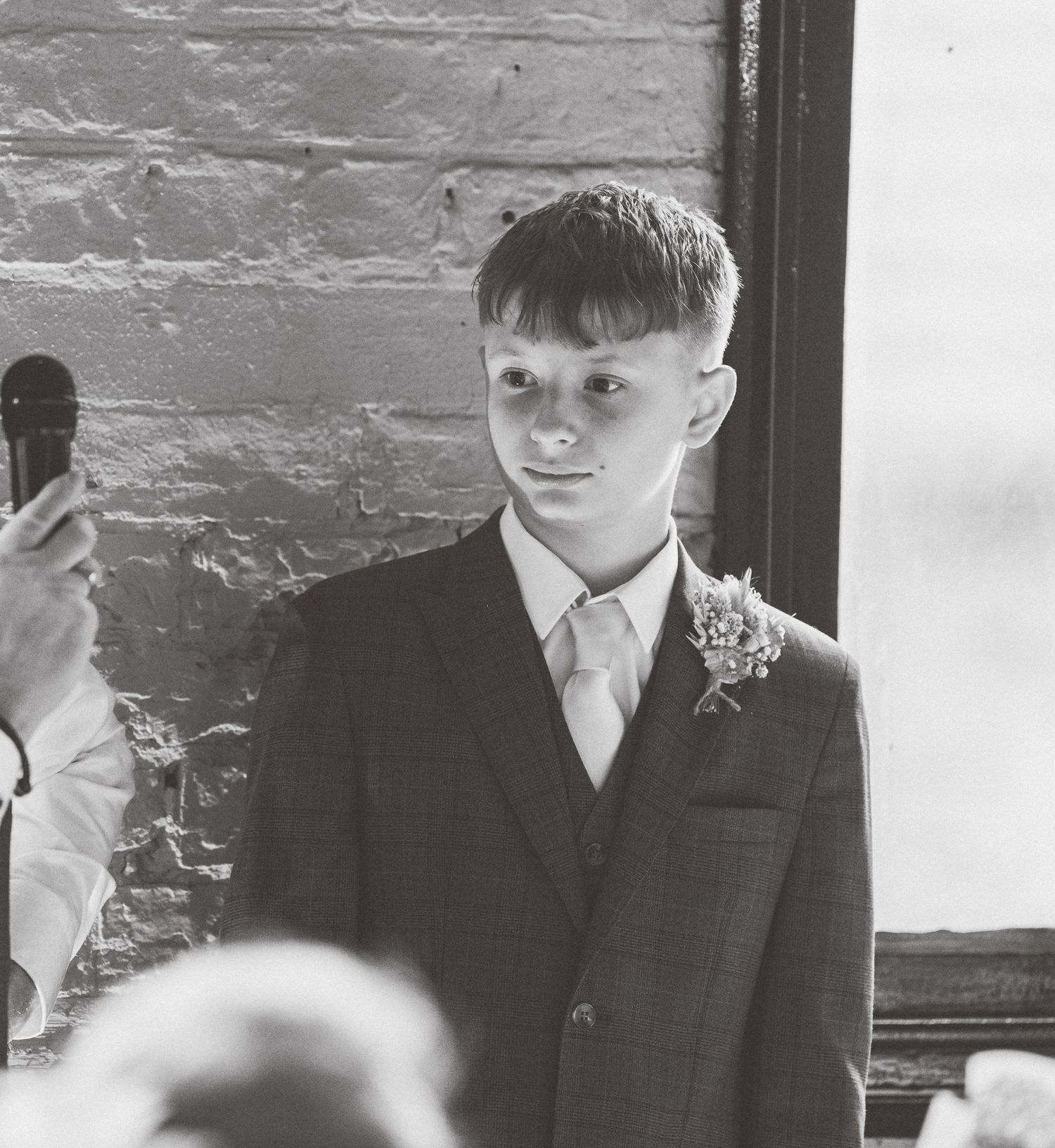 Black and white photo of formal-dressed attendants standing against painted brick wall.