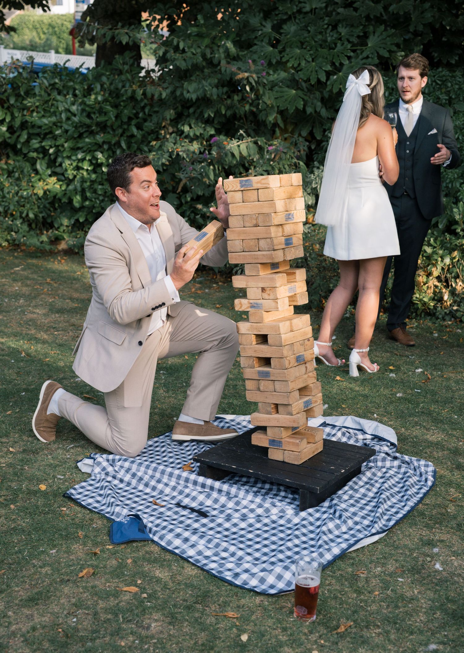 People playing giant Jenga on a checkered blanket during an outdoor event.