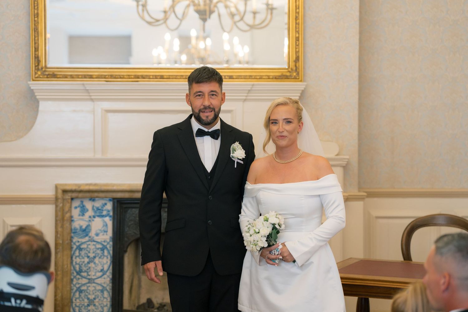 Bride and groom smiling together in elegant wedding attire inside a formal venue with chandelier.