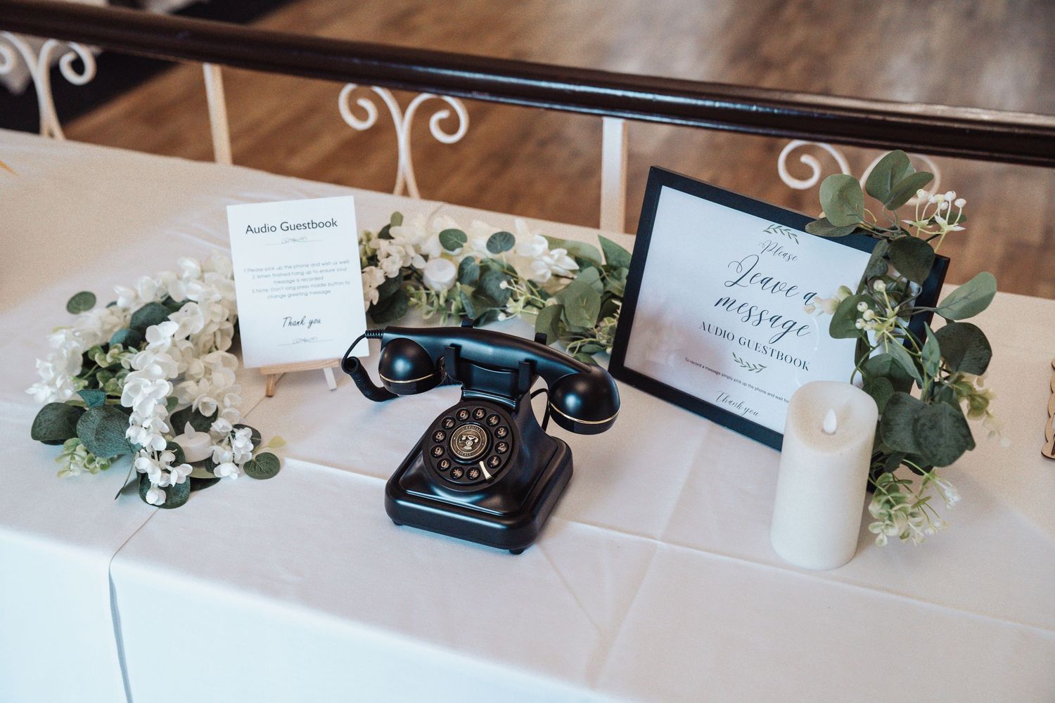 Vintage black rotary telephone with eucalyptus decor and candles on a white tablecloth at an elegant event.