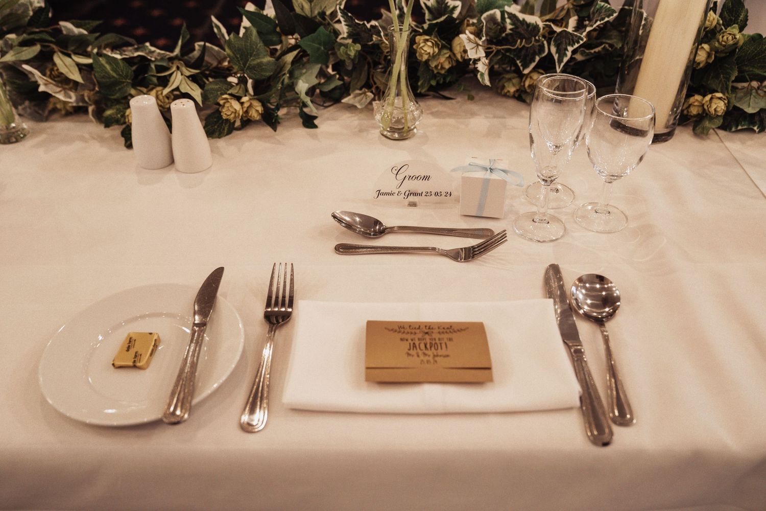 Elegant table setting with white linens, silverware, and greenery decorations at a formal event.