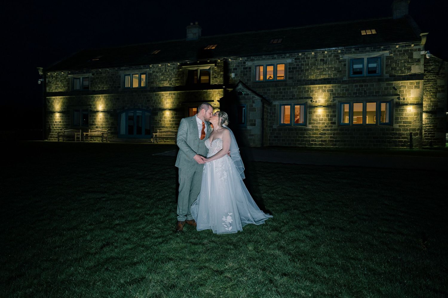A romantic nighttime wedding portrait with illuminated stone building in background.
