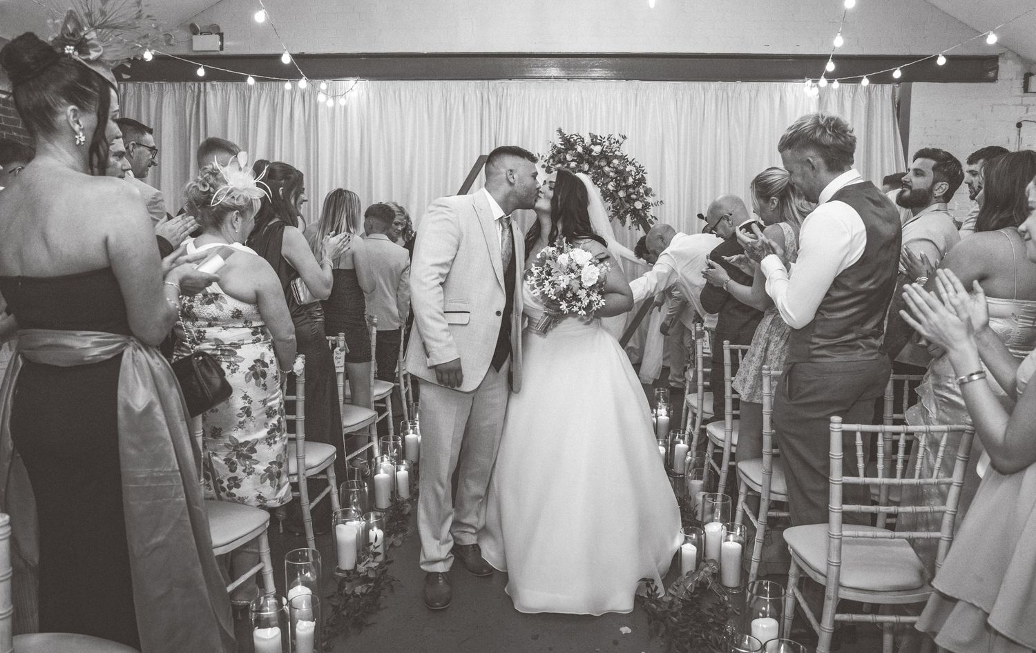 Black and white photo of a wedding ceremony with guests seated in rows and an elegant floral arch.