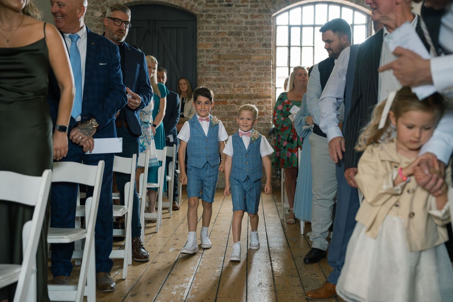 Wedding ceremony in a rustic brick venue with guests seated in white chairs.